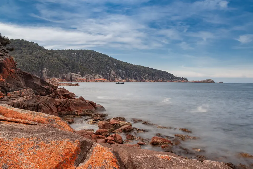 Orange-lichen granite rocks overlooking the sheltered water and forested coastline of Sleepy Bay, Freycinet National Park, Tasmania.