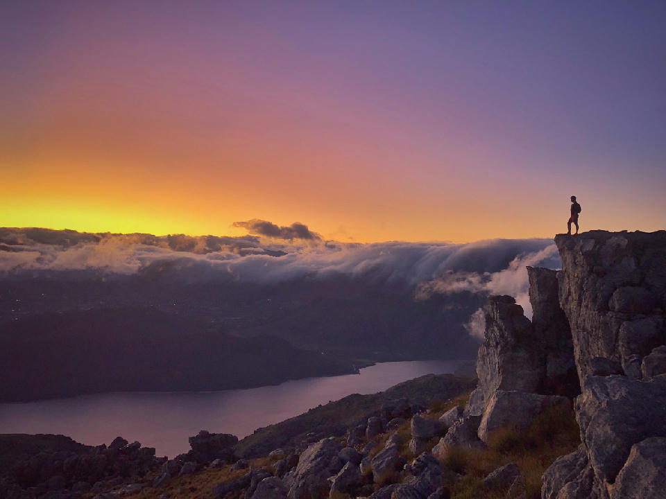 Trail runner on rocky summit overlooking mountain landscapes at dawn in Mont Rochelle Nature Reserve near Franschhoek, South Africa.