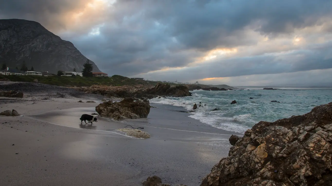 Moody coastal shoreline at Voëlklip Beach in Hermanus with rocky coves, surf, and storm clouds over Walker Bay