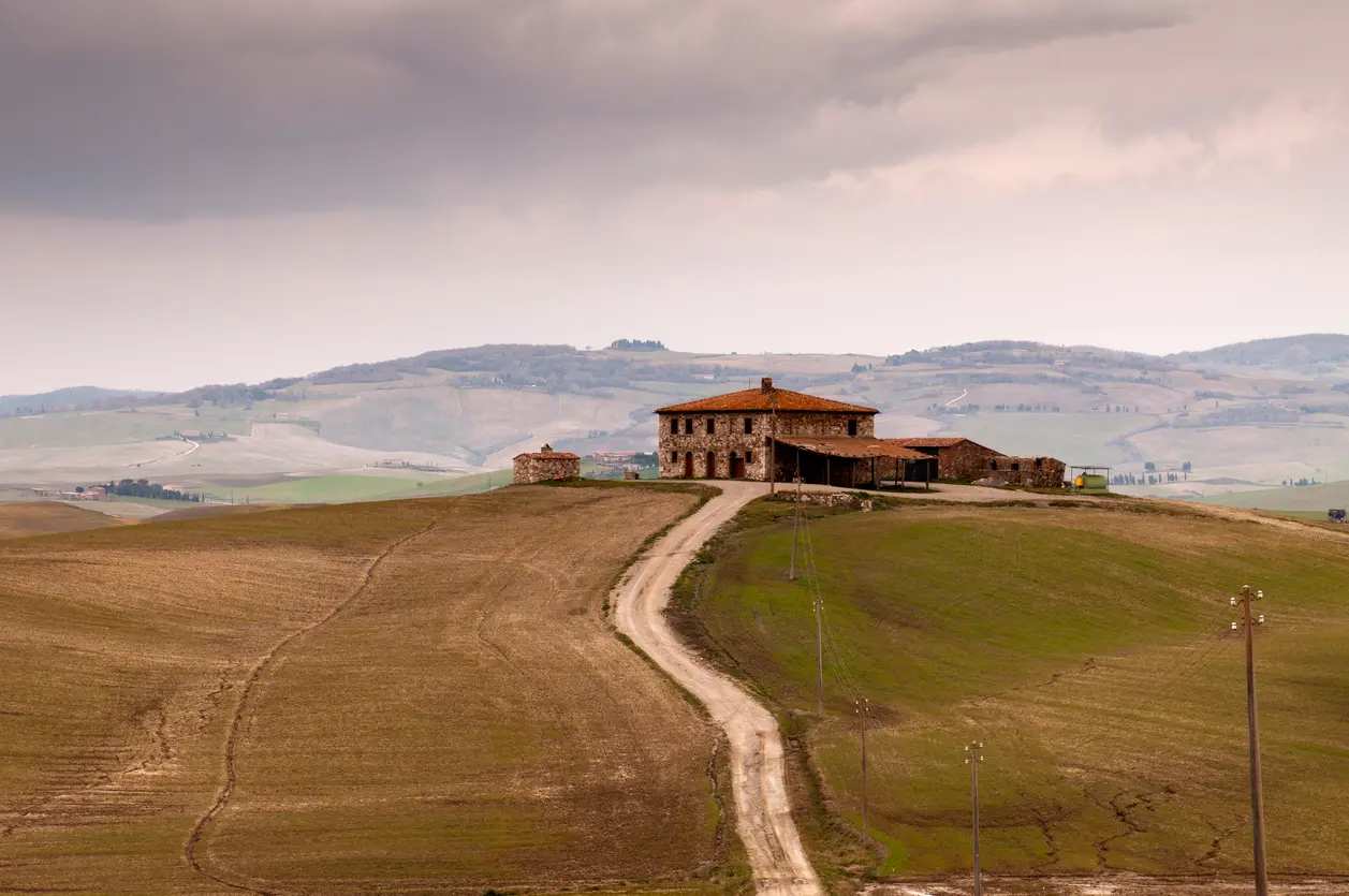 Farmhouse and winding dirt road at Podere Terrapille in the rolling hills of Val d’Orcia, Tuscany, Italy.