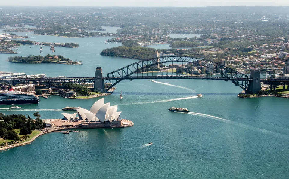 Aerial view of Sydney Harbour with the Sydney Opera House, Harbour Bridge and boats crossing the water.