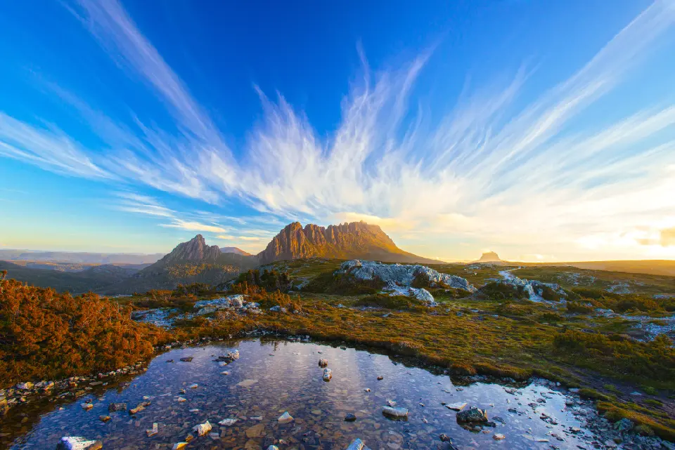 Cradle Mountain illuminated by warm evening light above alpine tarns and rocky moorland in Tasmania, Australia.
