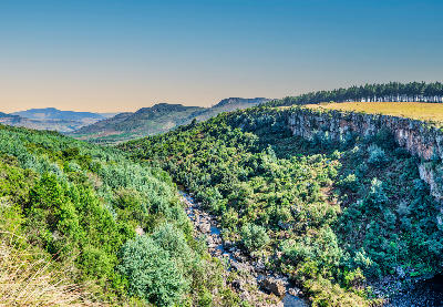 Wide view of the gorge below Berlin Falls with rocky escarpment cliffs, dense vegetation and a river valley in Mpumalanga.