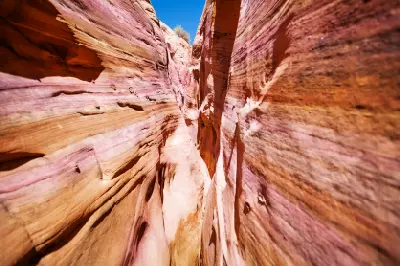 Colourful bands of red, pink and cream sandstone line the twisting narrow walls of Zebra Slot Canyon beneath a blue sky.