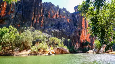 Green pool beneath towering dark rock walls streaked with orange at Dalmanyi (Bell Gorge) in the Kimberley.