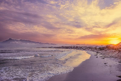 Sunrise over Long Beach in Kommetjie with soft waves, wide sand, and distant coastal hills along the Cape Peninsula.
