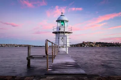 Bradleys Head Lighthouse at the end of its timber jetty, framed by pink sunset clouds over Sydney Harbour.