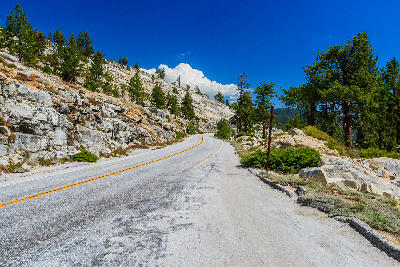 Ascending Tioga Pass Road bordered by exposed granite slabs and sparse pine trees in Yosemite National Park, California.