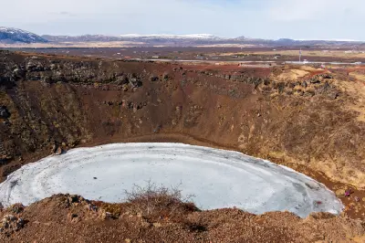 Kerið crater in Iceland with a frozen lake at the bottom and red volcanic slopes surrounding the circular caldera.