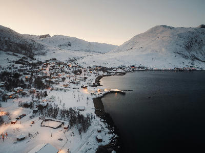Drone view of Ersfjord village and bay with snow-covered terrain, shoreline curve, and surrounding mountains