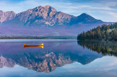 Yellow canoe floating on still Pyramid Lake with mountain reflections and forested shoreline