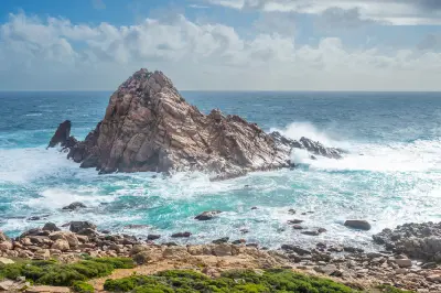 Sugarloaf Rock rising from turquoise water and heavy breaking surf near Cape Naturaliste in Western Australia.