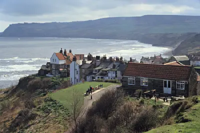 Robin Hood's Bay village overlooking the North Yorkshire coastline, with traditional cottages, breaking waves and Ravenscar cliffs in the distance.