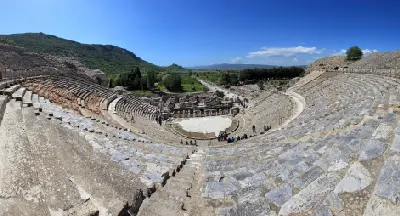Ancient semicircular stone seating of the Great Theatre of Ephesus overlooking the stage area and surrounding landscape beneath a clear blue sky.