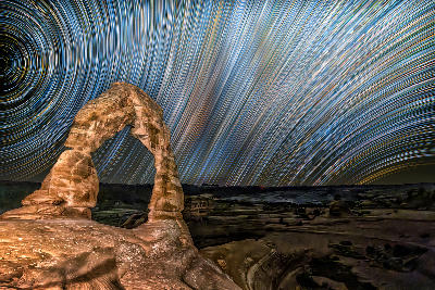 Delicate Arch illuminated at night with circular star trails in the sky in Arches National Park Utah