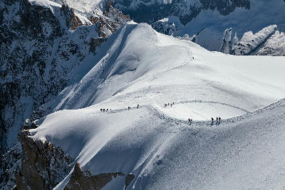 Climbers walking along a sharp snow ridge in the Mont Blanc Massif surrounded by high alpine peaks.
