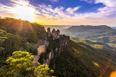 Golden sunrise light illuminates the Three Sisters sandstone formation above the forested Jamison Valley in the Blue Mountains.
