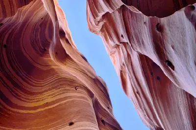 Looking upward between curved red and pink striped sandstone walls in Zebra Slot Canyon, Utah.