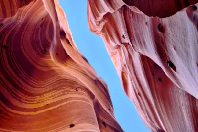 Looking upward between curved red and pink striped sandstone walls in Zebra Slot Canyon, Utah.