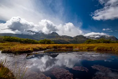 Alpine wetland and reflective pool at Key Summit with mountain peaks and clouds above Fiordland National Park, South Island, New Zealand.