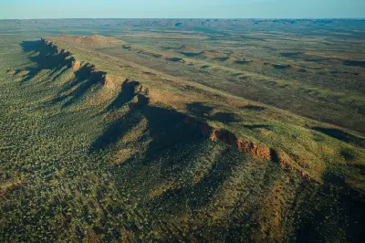 Low-angle sunlight casts long shadows across rugged escarpments and vast open wilderness near El Questro in the East Kimberley.