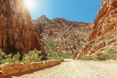 Gravel mountain road passing between towering sandstone cliffs in Swartberg Pass in the Klein Karoo of South Africa.
