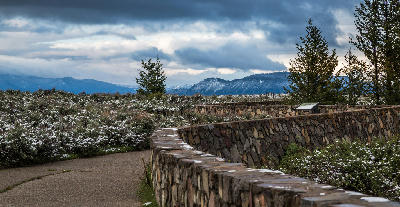 Stone viewing wall and path at Snake River Overlook with light snow on vegetation and mountains under heavy clouds, Grand Teton National Park, Wyoming.