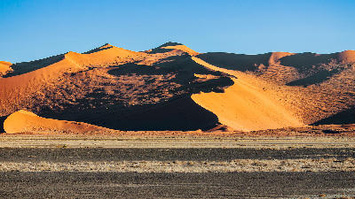 Orange Namib sand dunes with dramatic black shadow slopes and sharp crest lines in Sossusvlei, Namibia.