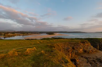 Morning view across the Minnamurra River mouth and sweeping sandbar toward the ocean, framed by grassy coastal headlands.