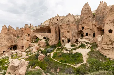 Ancient rock-cut cave dwellings and fairy chimney formations at Zelve Open Air Museum in Cappadocia, Turkey, with walking paths winding through the historic monastic settlement.