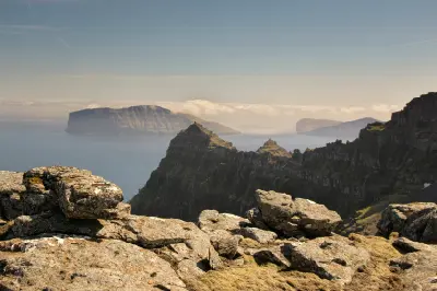 Rocky foreground at Enniberg overlooking steep cliffs and the North Atlantic with Fugloy and Svínoy islands in the distance, Faroe Islands.