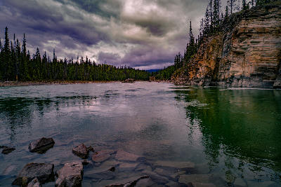 Athabasca River flowing past rocky cliffs and forest under dramatic cloudy sky