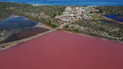 Aerial view of pink Hutt Lagoon beside Port Gregory and the blue Indian Ocean.