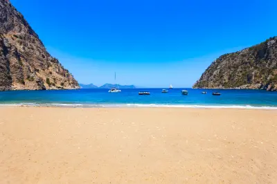 View from Butterfly Valley Beach across turquoise water and boats between towering coastal cliffs near Ölüdeniz, Türkiye.