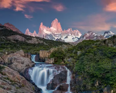 Waterfall in the foreground with Mount Fitz Roy illuminated by pink light in Patagonia, Argentina.