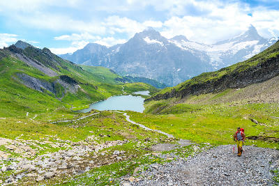 Mountain trail descending toward Bachalpsee with a hiker, overlooking the twin alpine lakes and surrounding green slopes near Grindelwald, Switzerland.