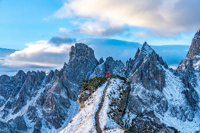 Hiker on Cadini di Misurina ridge viewpoint with Dolomite spires behind, Italy.