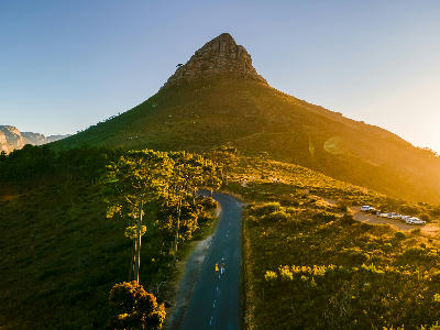 Golden sunset illuminating Lion’s Head mountain with road and small figures below in Cape Town, South Africa.