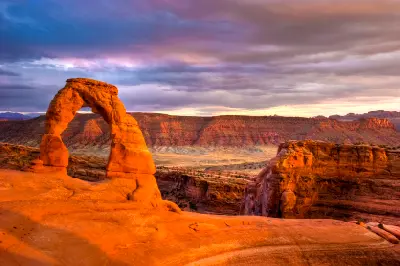 Delicate Arch silhouetted against a sunset sky above desert canyon in Arches National Park Utah
