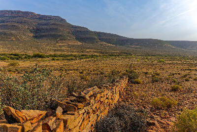 Historic stone wall crossing the arid Biedouw Valley beneath towering sandstone escarpments in the northern Cederberg of South Africa.