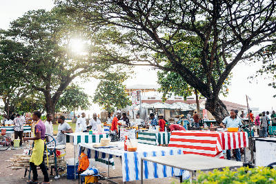 Food vendors preparing stalls beneath shady trees at the Forodhani Gardens evening market in Stone Town, Zanzibar.