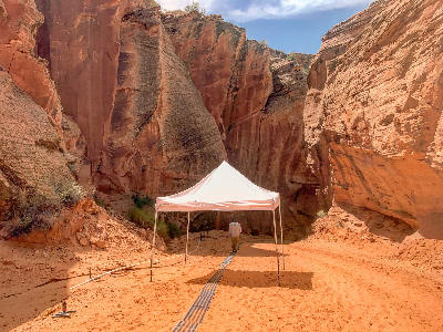 Canyon X entrance in Page, Arizona with white canopy tent and sandy path leading into tall red sandstone canyon walls.