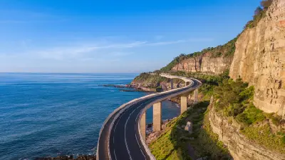Sweeping aerial view of Sea Cliff Bridge curving between steep sandstone cliffs and the blue Pacific Ocean on the Illawarra coast.