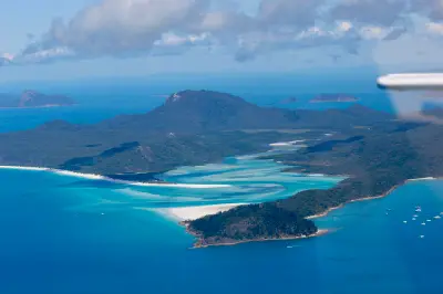 Distant aerial view of Whitehaven Beach and Hill Inlet surrounded by forested Whitsunday Islands, Queensland, Australia.