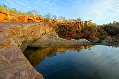 Still rock pool above Bell Gorge reflects warm sandstone cliffs and native vegetation in the Kimberley.