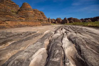 Deep erosion channels carved into the dry bed of Piccaninny Creek lead toward the striped sandstone domes of the Bungle Bungle Range.