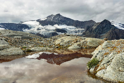Small alpine reflection pool with glacier and rocky peaks in the background in Vanoise National Park