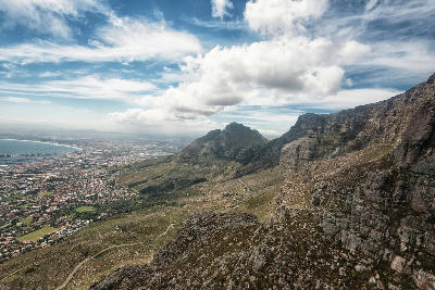 Rocky cliffs of Table Mountain in the foreground looking toward Devil’s Peak and Cape Town suburbs and coastline below.