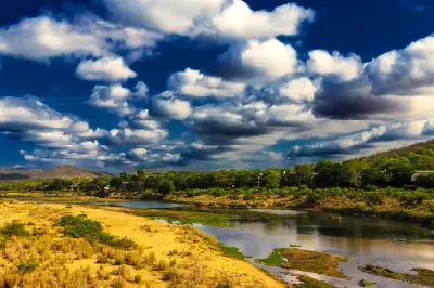 Dramatic storm clouds over the Crocodile River near Malelane Gate in southern Kruger National Park, with sandy riverbanks and bushveld vegetation.