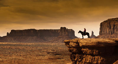 A rider on horseback silhouetted against sandstone buttes in Monument Valley, part of the Southwest United States desert landscape.